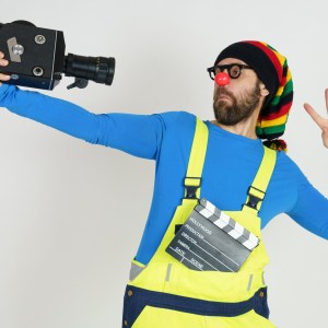 Celebration and communication concept. A clown in bright clothes filming himself with a movie camera. Isolated on white