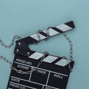 Movie clapperboard wrapped in steel chain on blue background. Ban on filmmaking. Top view