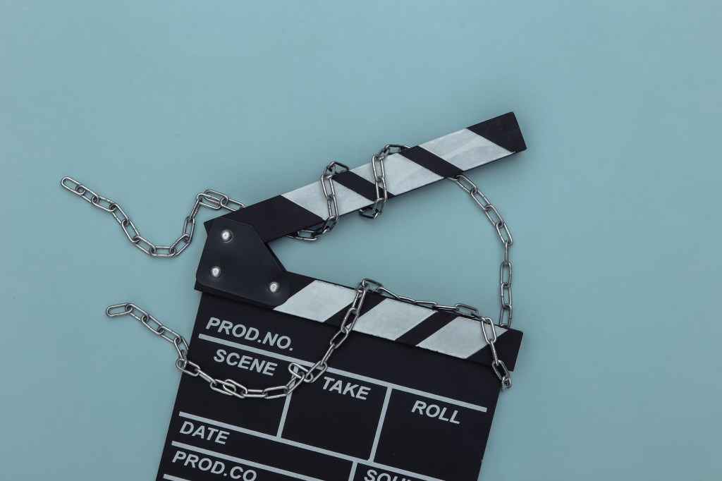 Movie clapperboard wrapped in steel chain on blue background. Ban on filmmaking. Top view Movie clapperboard wrapped in steel chain on blue background. Ban on filmmaking. Top view