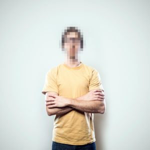 A portrait of a hipster young man from the waist up, whose face has been rendered unrecognizable by being pixelated.  A conceptual representation of individual identity protection.  Square crop with copy space on a a clean off-white background.