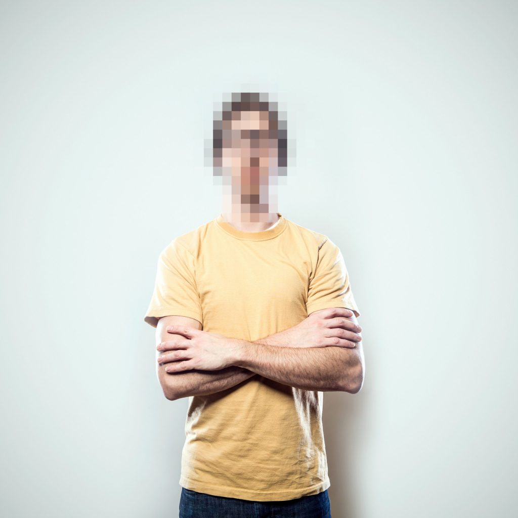 A portrait of a hipster young man from the waist up, whose face has been rendered unrecognizable by being pixelated.  A conceptual representation of individual identity protection.  Square crop with copy space on a a clean off-white background.