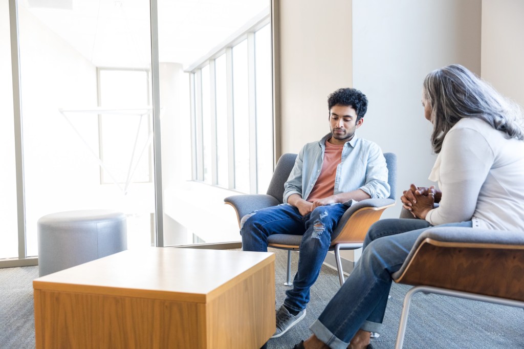 The young adult male student looks down at the floor and pauses to think of how he wants to answer the counselor's question.