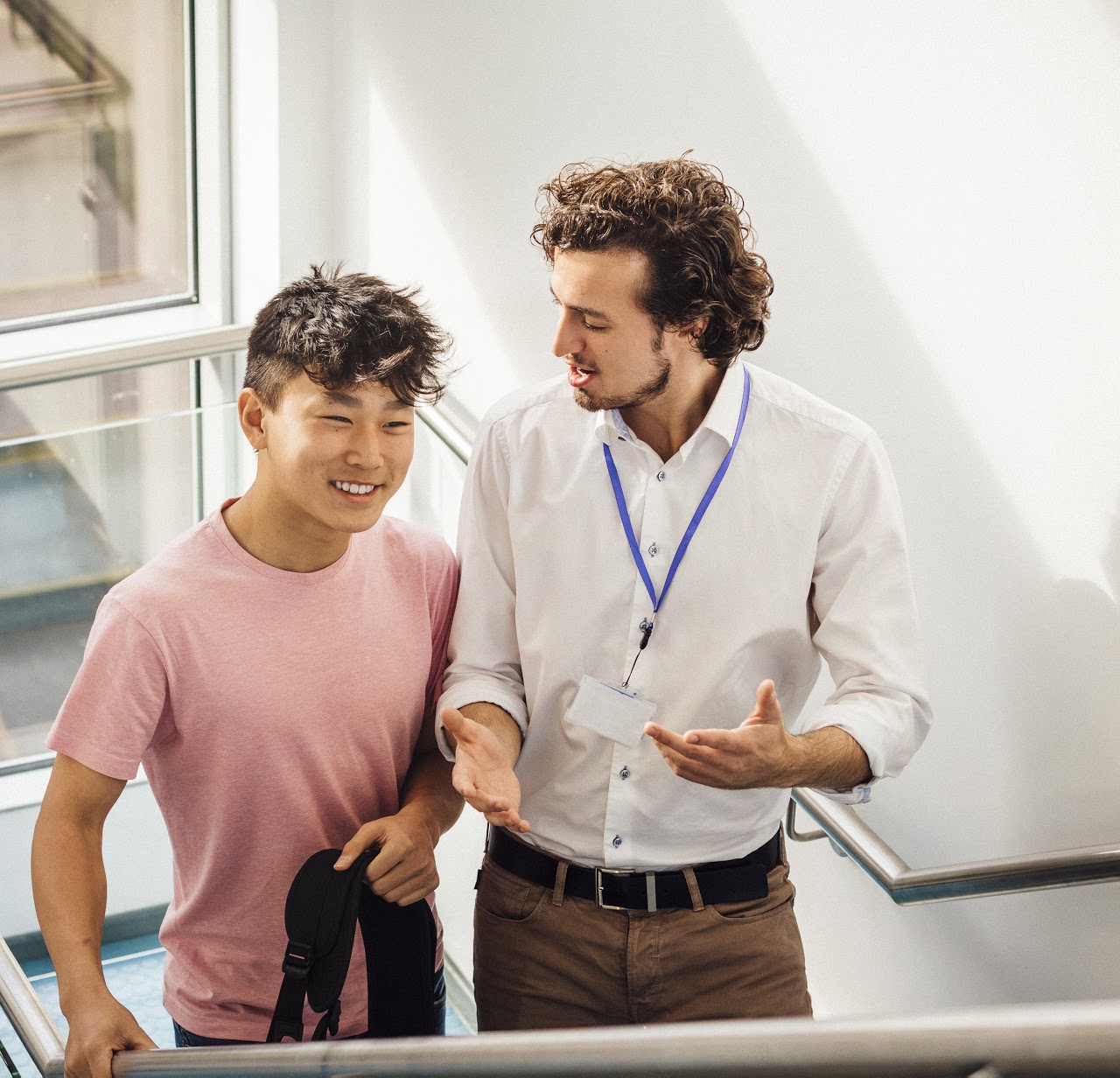 Student and his teacher make their way up the school staircase. They look happy as they talk.