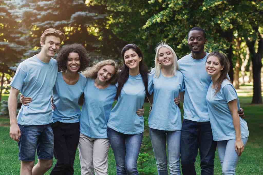 Group of happy young diverse volunteers embracing at park, ready for work, copy space