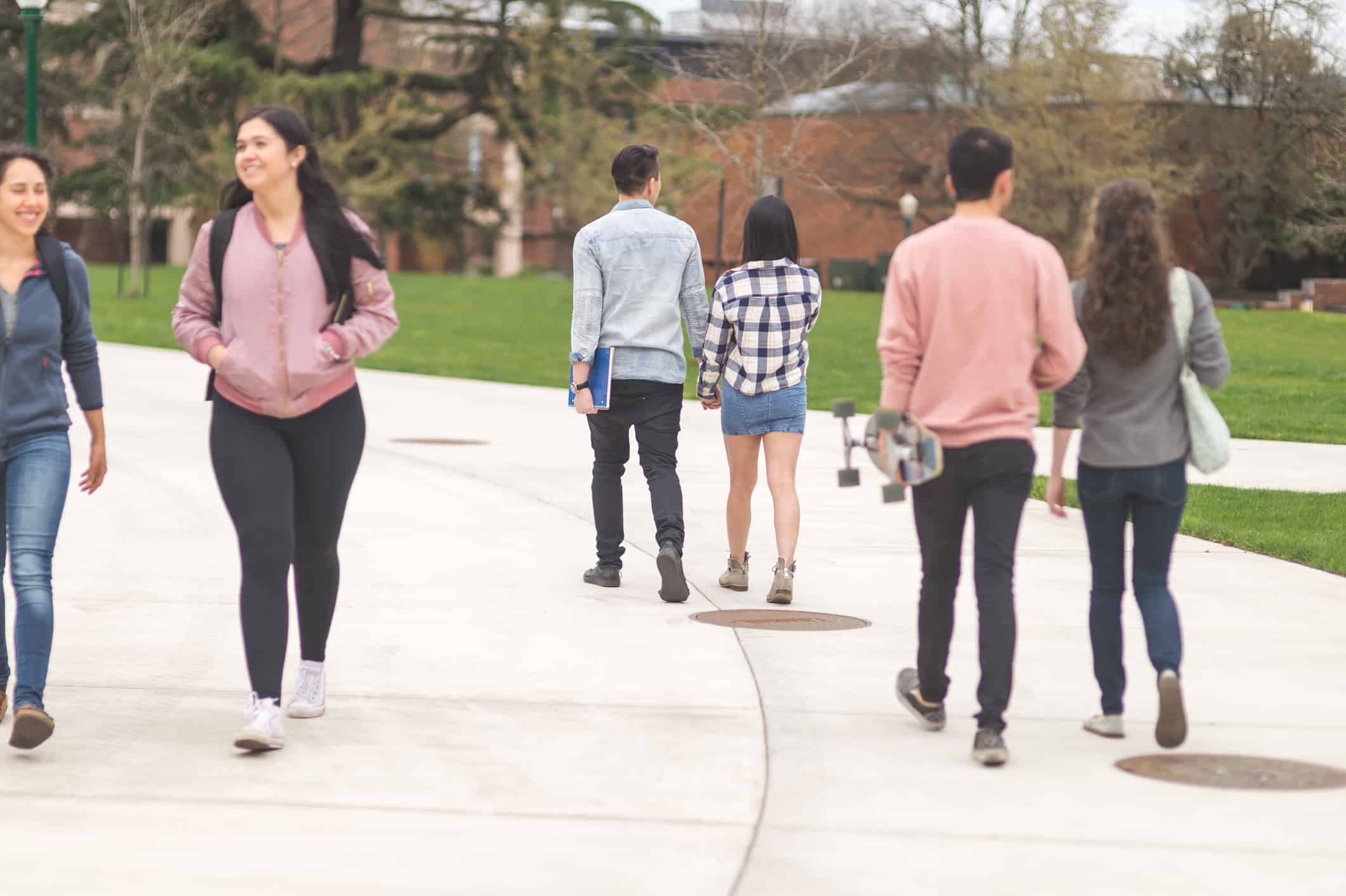 Multiethnic college students walk on the sidewalk across campus to their next classes on a spring afternoon.